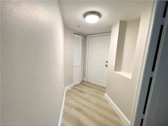 Bright and welcoming entrance featuring freshly painted walls, modern baseboards, light wood-style flooring, a decorative niche, and a convenient utility closet.