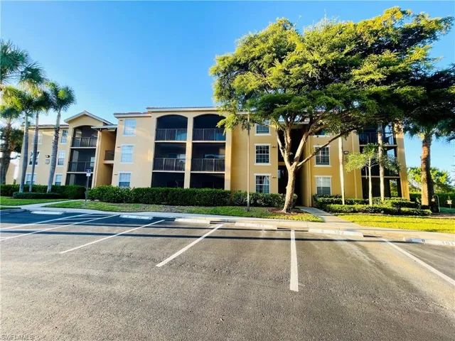 Detailed exterior shot showcasing a nicely kept condominium building situated with a picturesque lakeside view, also featuring uncovered parking areas for residents and visitors.