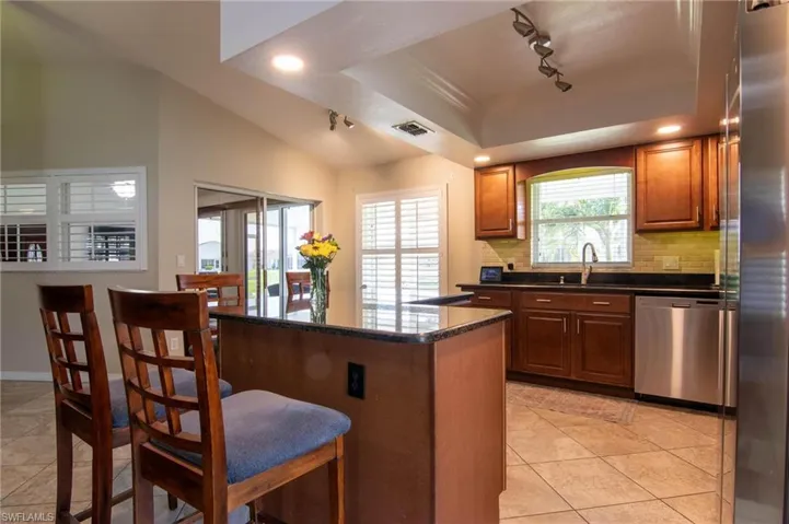 Kitchen featuring track lighting, stainless steel appliances, a kitchen bar, light tile patterned floors, and decorative backsplash