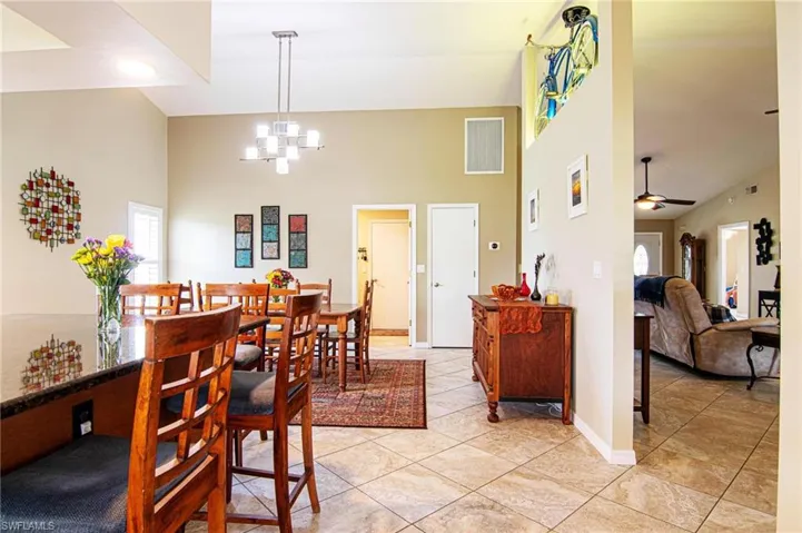 Dining area with high vaulted ceiling, light tile patterned floors, a chandelier, and a ceiling fan