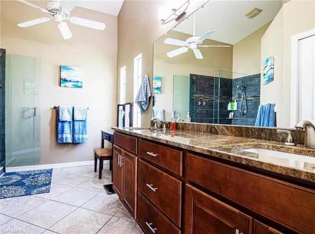 Full bathroom featuring a ceiling fan, a stall shower, double vanity, tile patterned floors, and high vaulted ceiling