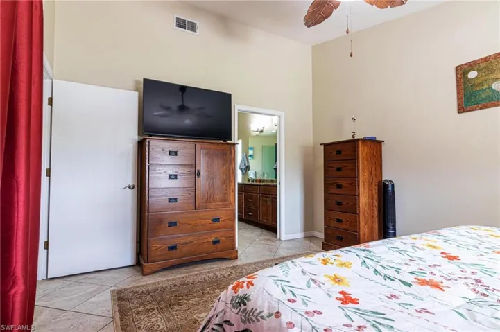 Bedroom with light tile patterned floors, connected bathroom, and a ceiling fan