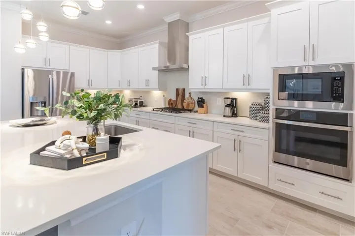 Kitchen with wall chimney exhaust hood, white cabinetry, appliances with stainless steel finishes, and pendant lighting