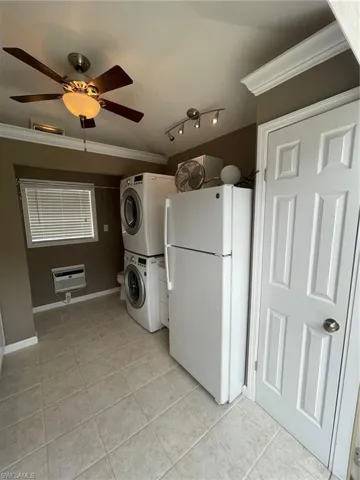 Laundry area featuring ceiling fan, light tile floors, stacked washer and dryer, rail lighting, and ornamental molding