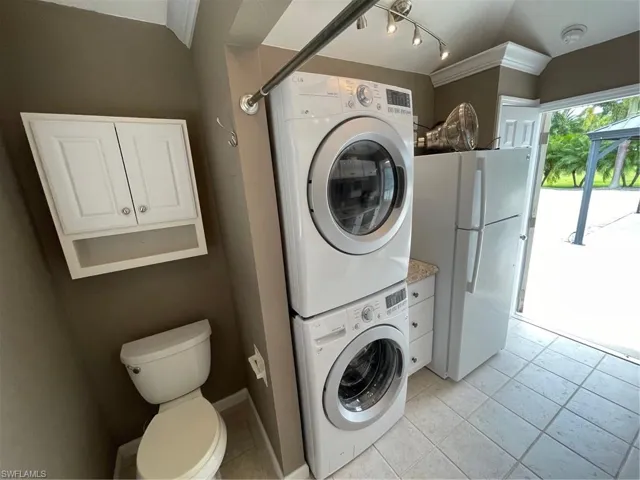 Clothes washing area with stacked washing maching and dryer, light tile flooring, and track lighting