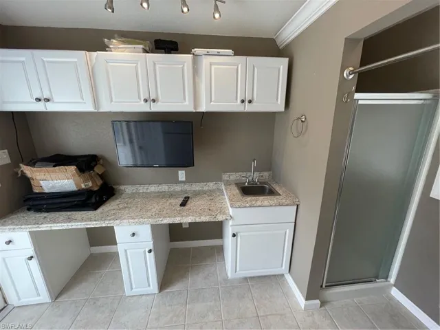 Kitchen featuring sink, white cabinetry, ornamental molding, and light tile floors