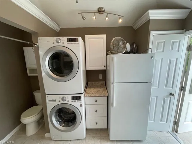 Washroom with stacked washer / drying machine, track lighting, ornamental molding, and light tile floors