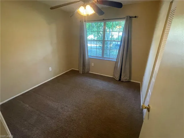 Unfurnished room featuring dark carpet, ceiling fan, and baseboards