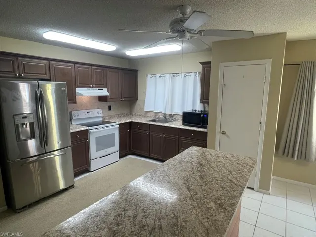 Kitchen featuring electric stove, stainless steel fridge, under cabinet range hood, black microwave, and a ceiling fan