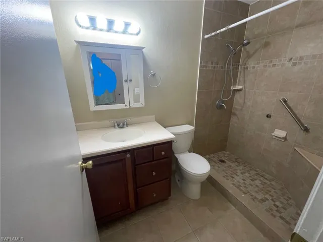 Bathroom with tile patterned floors, tiled shower, toilet, and vanity