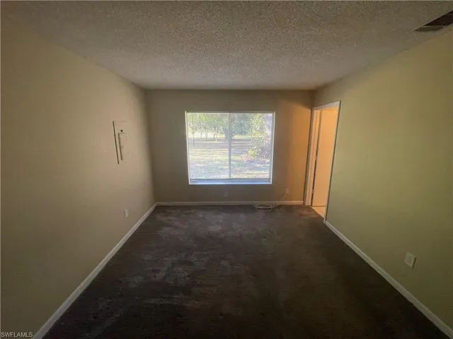 Unfurnished room with a textured ceiling, visible vents, dark colored carpet, and baseboards
