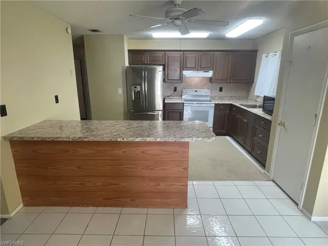 Kitchen with ceiling fan, under cabinet range hood, white electric range, a peninsula, and stainless steel fridge