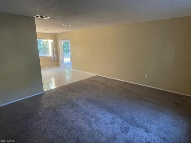 Tiled spare room with an inviting chandelier, carpet, visible vents, and baseboards