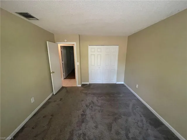 Unfurnished bedroom with a textured ceiling, visible vents, a closet, baseboards, and carpet