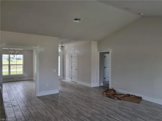 Spare room featuring dark wood-type flooring, lofted ceiling, and an inviting chandelier