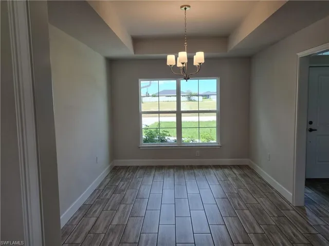 Empty room featuring a raised ceiling, dark hardwood / wood-style floors, and a chandelier