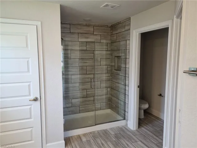 Bathroom featuring hardwood / wood-style floors, toilet, and an enclosed shower