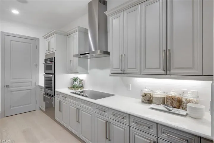 Kitchen with electric stovetop, wall chimney range hood, a warming drawer, and light countertops