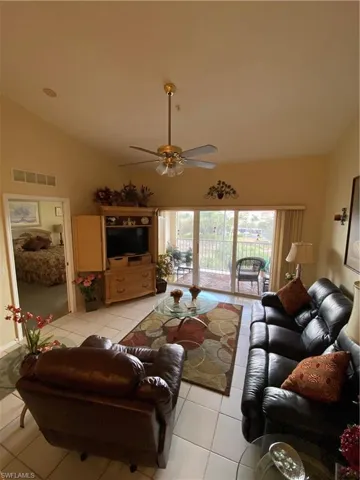 Living area with ceiling fan, light tile patterned flooring, and vaulted ceiling