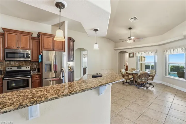 Kitchen with appliances with stainless steel finishes, hanging light fixtures, dark stone counters, a ceiling fan, and brown cabinets