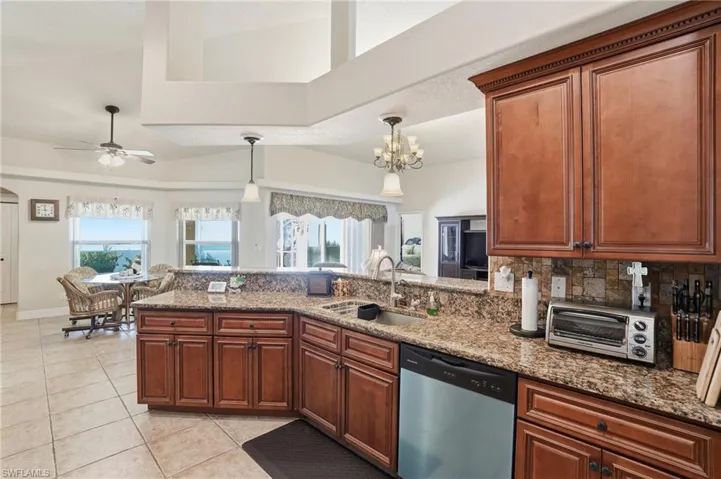 Kitchen with a peninsula, stainless steel dishwasher, light stone counters, and brown cabinets