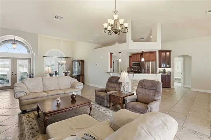 Living room with a chandelier, arched walkways, french doors, light tile patterned floors, and high vaulted ceiling