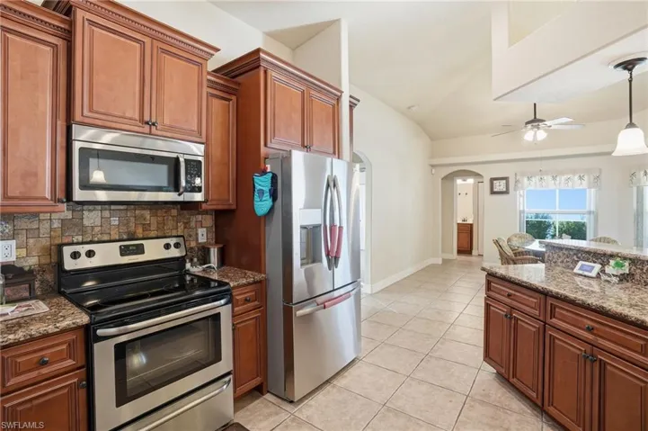 Kitchen with stainless steel appliances, dark stone countertops, arched walkways, brown cabinets, and vaulted ceiling
