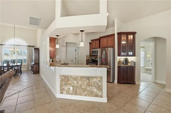 Kitchen with arched walkways, stainless steel appliances, pendant lighting, light stone countertops, and high vaulted ceiling