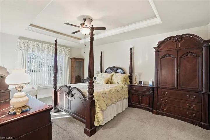 Bedroom featuring a tray ceiling, light carpet, ceiling fan, and crown molding