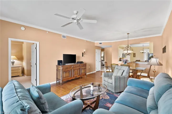 Living room with ornamental molding, ceiling fan with notable chandelier, and light wood-type flooring