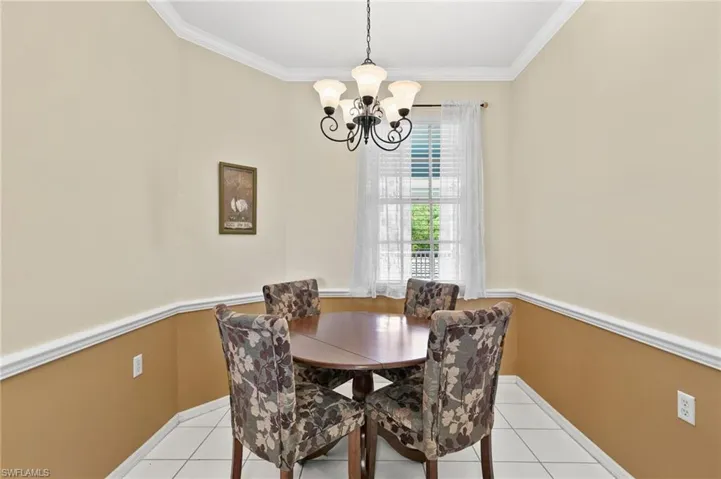 Dining room with a notable chandelier, ornamental molding, and light tile floors