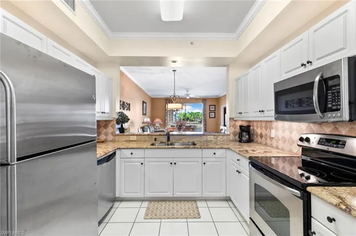 Kitchen with crown molding, stainless steel appliances, white cabinets, backsplash, and sink