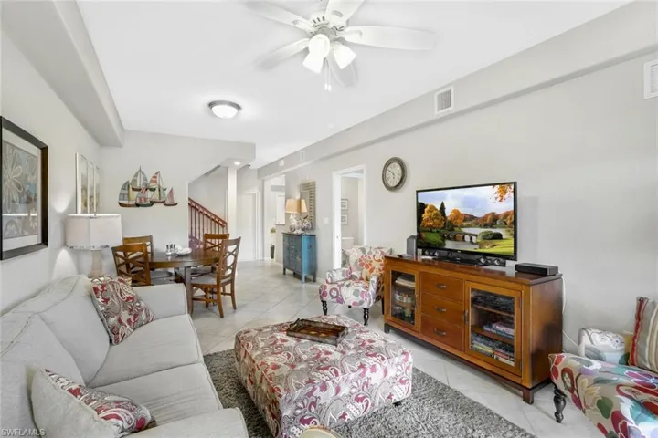 Living area featuring light tile patterned floors, a ceiling fan, and stairs