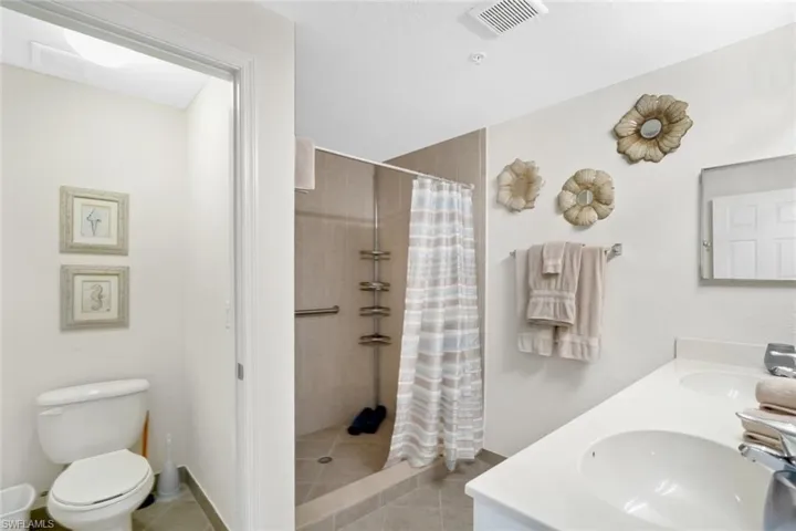 Full bathroom featuring tiled shower, tile patterned floors, toilet, and double vanity