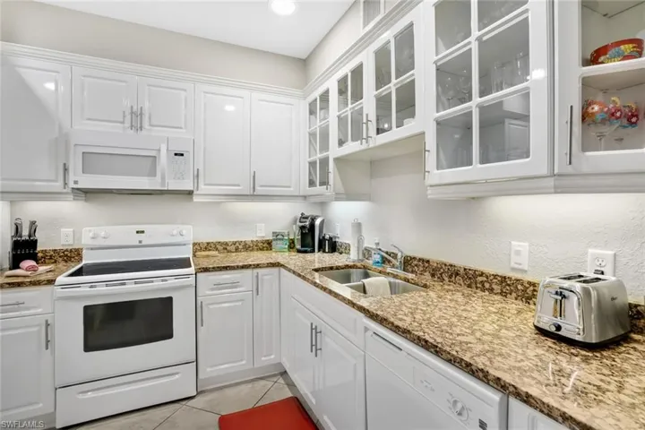 Kitchen featuring white appliances, white cabinetry, a sink, and glass insert cabinets