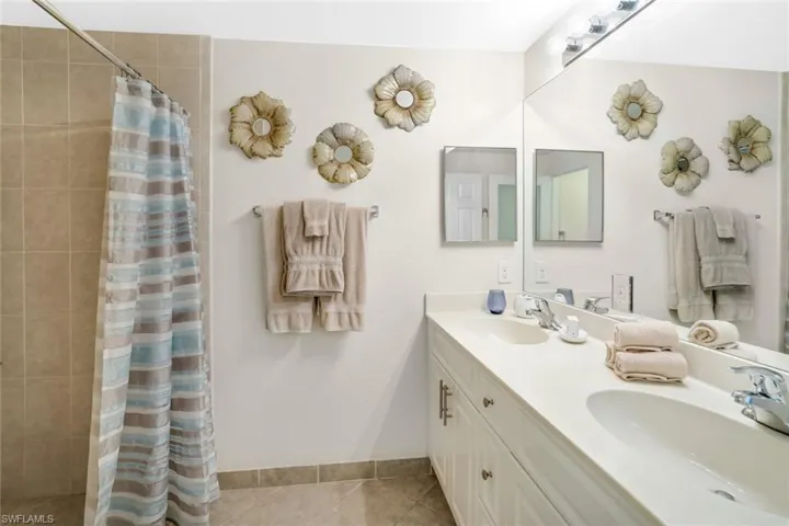 Full bath featuring tiled shower, tile patterned floors, double vanity, and baseboards