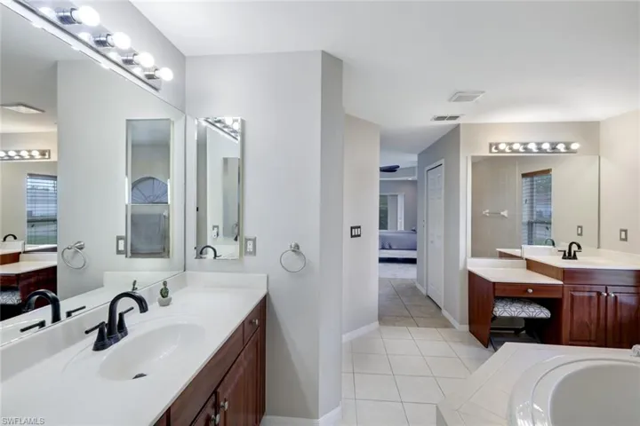 Full bath with light tile patterned floors, ensuite bath, two vanities, and a garden tub