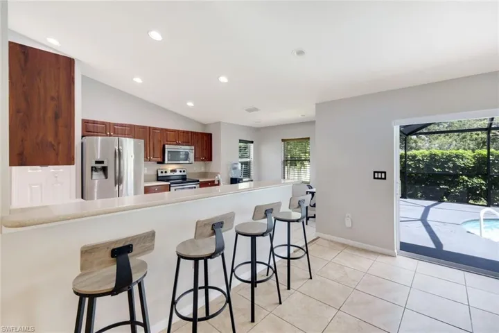 Kitchen with a breakfast bar area, a peninsula, stainless steel appliances, light tile patterned floors, and recessed lighting