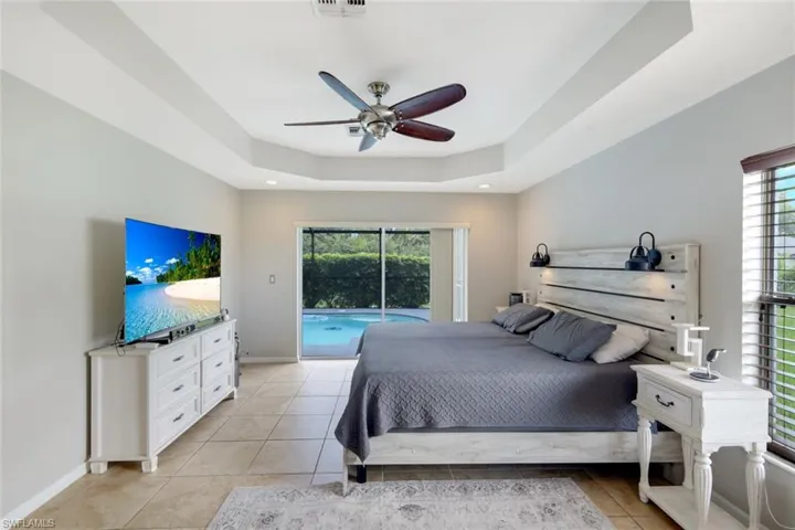 Bedroom with a raised ceiling, access to exterior, multiple windows, and a ceiling fan