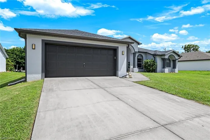 Single story home featuring a front yard, driveway, stucco siding, and an attached garage