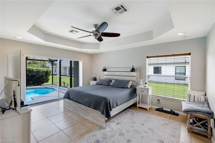 Bedroom with light tile patterned floors, a raised ceiling, access to exterior, ceiling fan, and recessed lighting
