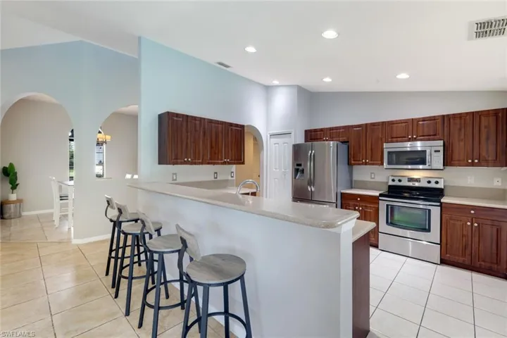 Kitchen with arched walkways, vaulted ceiling, stainless steel appliances, light tile patterned floors, and light countertops