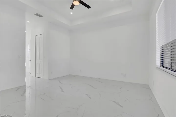 Empty room with a raised ceiling, light marble finish flooring, ceiling fan, and recessed lighting