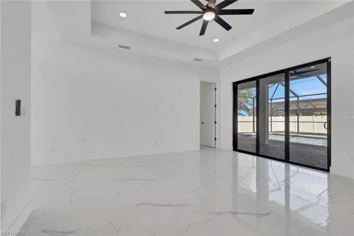 Empty room with a raised ceiling, ceiling fan, light marble finish floors, and recessed lighting