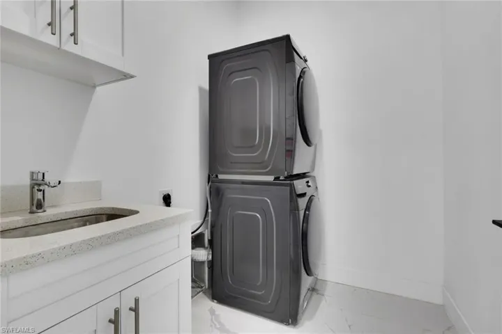 Laundry room featuring cabinet space, stacked washer and dryer, and light marble finish floors