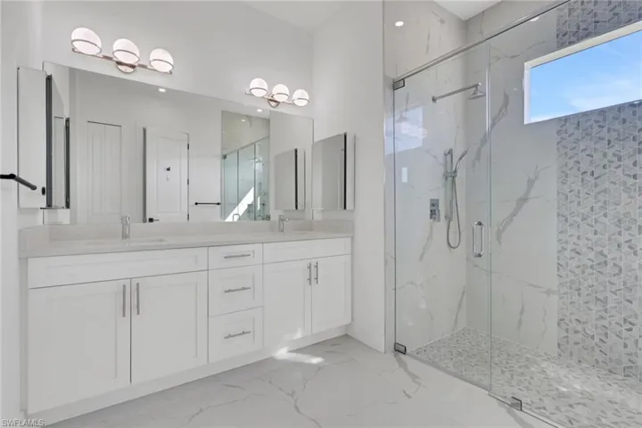 Bathroom with double vanity, a marble finish shower, and light marble finish flooring