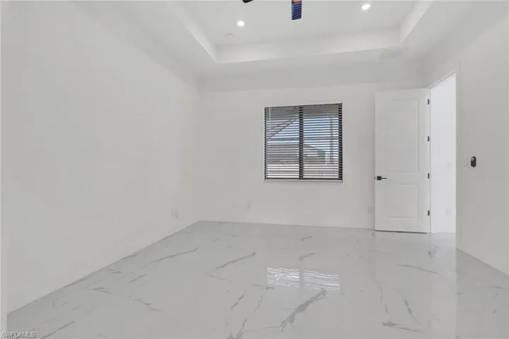 Spare room with a raised ceiling, light marble finish floors, ceiling fan, and recessed lighting