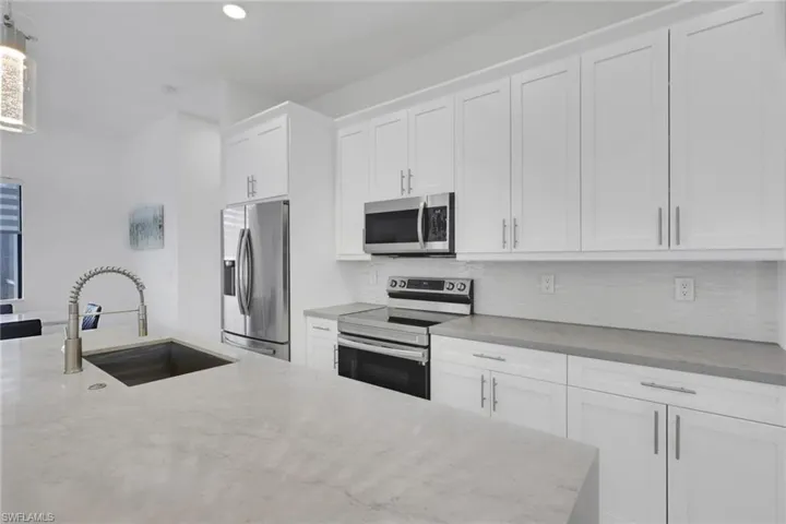 Kitchen with stainless steel appliances, white cabinetry, light stone countertops, pendant lighting, and backsplash