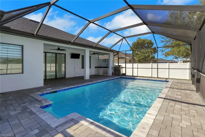 View of pool with a sunroom, exterior kitchen, a lanai, and patio surround