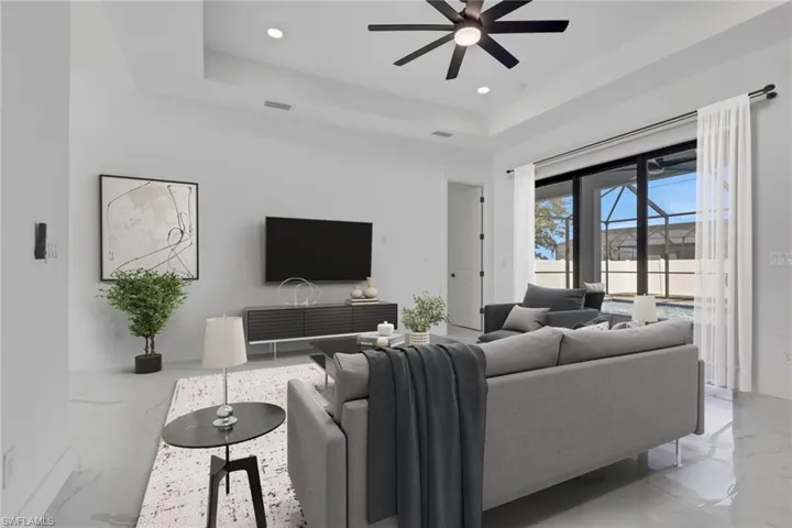 Living area with a tray ceiling, light marble finish flooring, a ceiling fan, and recessed lighting